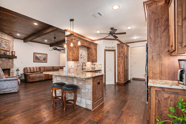 kitchen featuring dark wood-type flooring, sink, beam ceiling, light stone counters, and kitchen peninsula