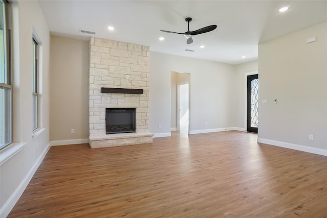 unfurnished living room featuring a stone fireplace, hardwood / wood-style floors, and ceiling fan