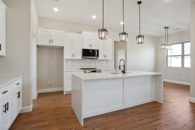 kitchen featuring stainless steel appliances, a center island with sink, sink, white cabinetry, and hanging light fixtures