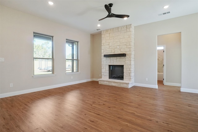 unfurnished living room featuring a stone fireplace, hardwood / wood-style floors, and ceiling fan