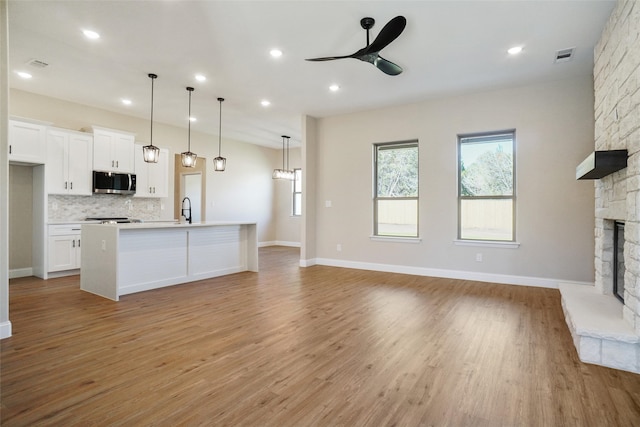 kitchen featuring white cabinetry, decorative light fixtures, an island with sink, a stone fireplace, and light hardwood / wood-style flooring