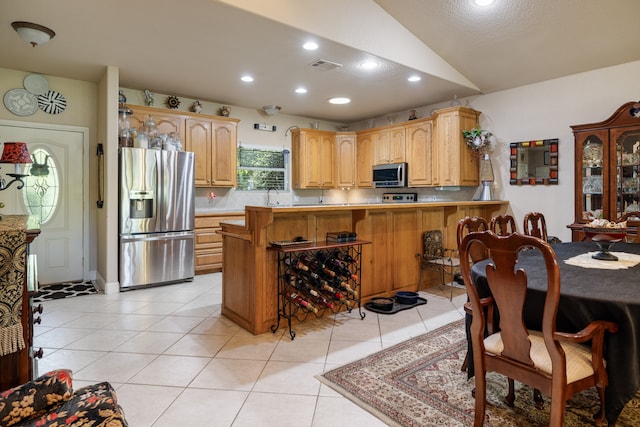 kitchen featuring lofted ceiling, light tile patterned floors, stainless steel appliances, a kitchen bar, and kitchen peninsula