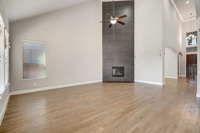 unfurnished living room with a tiled fireplace, light hardwood / wood-style floors, a high ceiling, and ceiling fan with notable chandelier