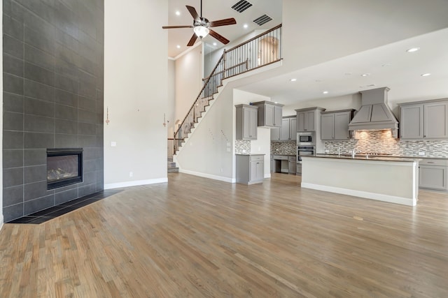 unfurnished living room with a high ceiling, sink, light wood-type flooring, a fireplace, and ceiling fan