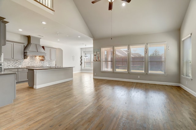 unfurnished living room with light hardwood / wood-style flooring, high vaulted ceiling, sink, and ceiling fan