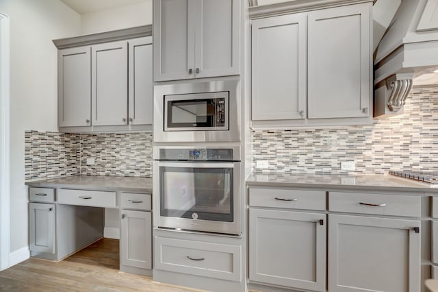 kitchen featuring decorative backsplash, appliances with stainless steel finishes, light stone countertops, light hardwood / wood-style flooring, and gray cabinetry