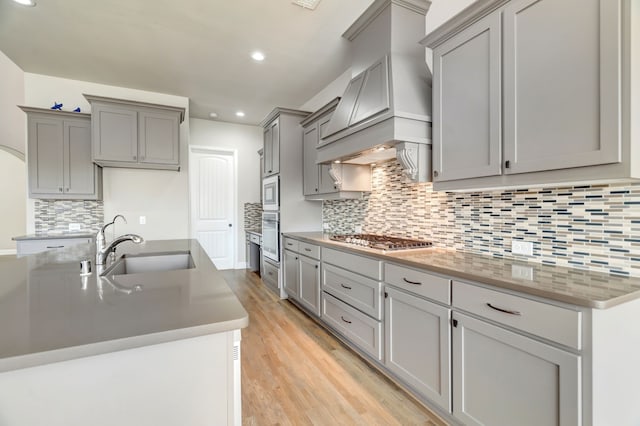 kitchen with gray cabinetry, backsplash, sink, light wood-type flooring, and appliances with stainless steel finishes