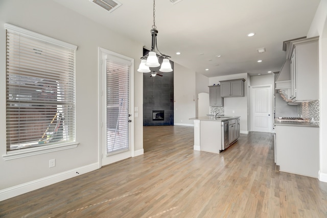 kitchen with a kitchen island with sink, light hardwood / wood-style flooring, gray cabinetry, decorative light fixtures, and tasteful backsplash