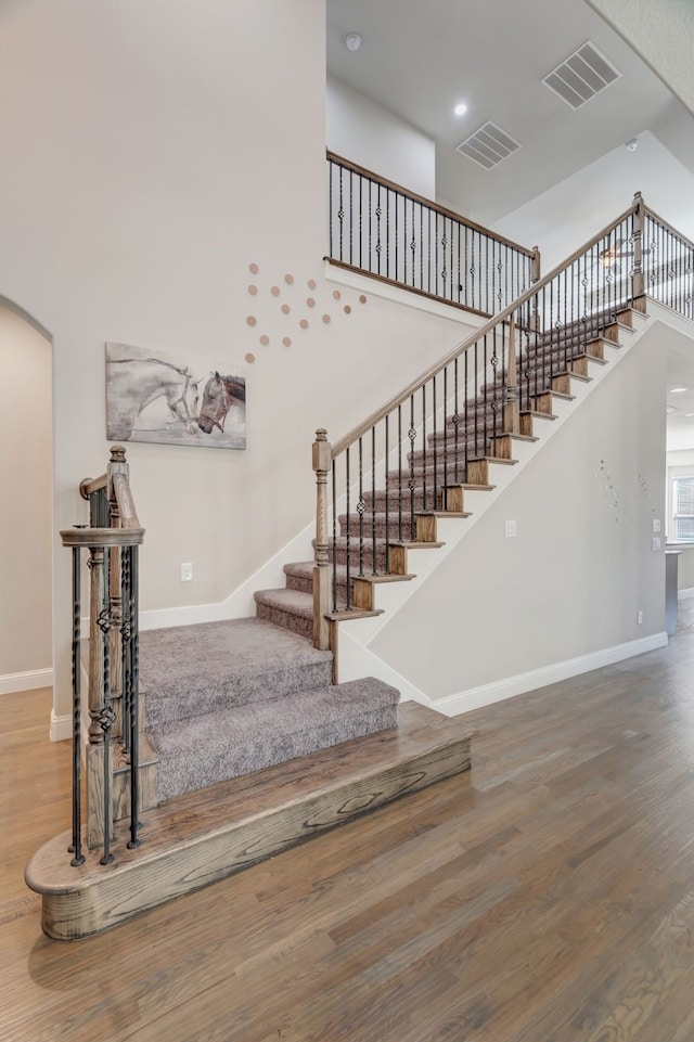 staircase featuring a towering ceiling and wood-type flooring