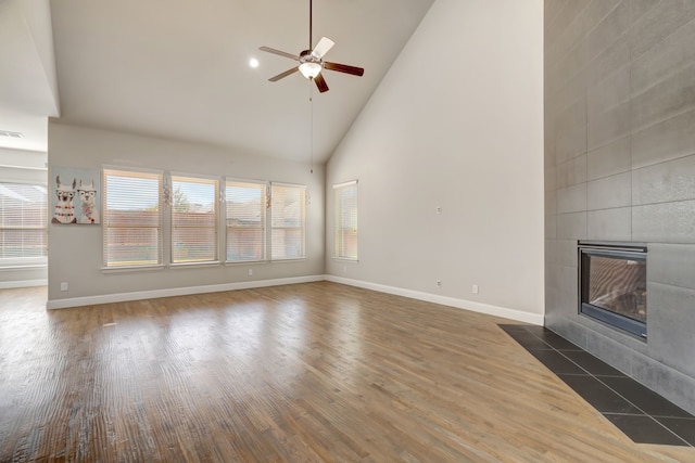 unfurnished living room with a tile fireplace, dark wood-type flooring, high vaulted ceiling, and ceiling fan