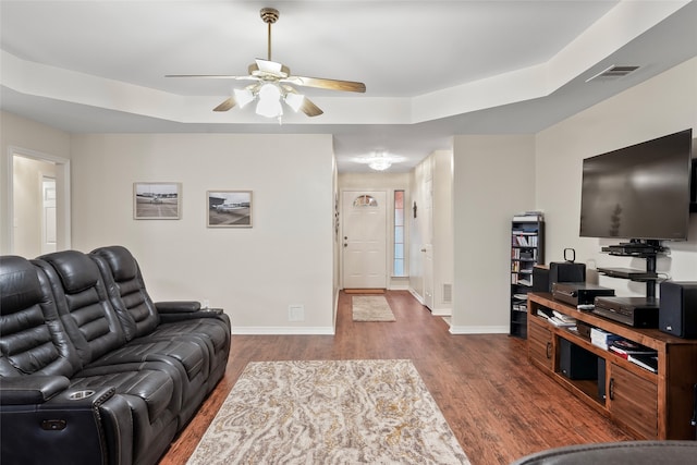 living room with a tray ceiling, wood-type flooring, and ceiling fan