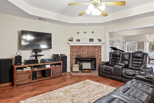 living room featuring a raised ceiling, hardwood / wood-style floors, a fireplace, and ceiling fan