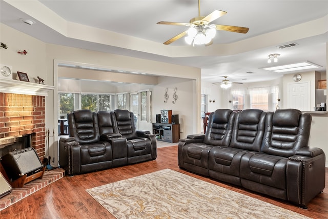 cinema room featuring a brick fireplace, wood-type flooring, and ceiling fan