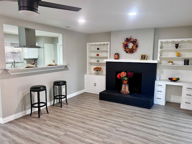 kitchen featuring white cabinetry, stainless steel stove, island range hood, light wood-type flooring, and sink