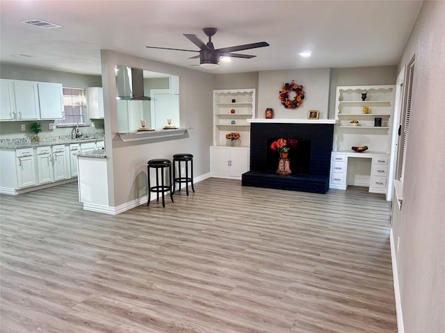 kitchen featuring gas stove, white cabinetry, light hardwood / wood-style floors, light stone counters, and ventilation hood