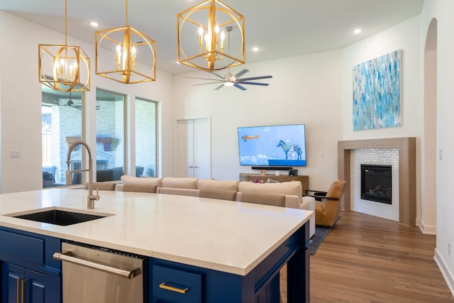 kitchen with dishwasher, a tile fireplace, sink, blue cabinetry, and a center island with sink