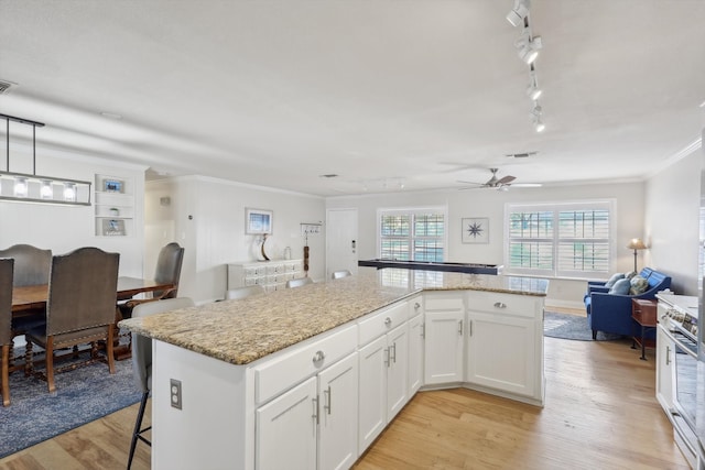 kitchen with a kitchen island, white cabinetry, decorative light fixtures, light stone counters, and light hardwood / wood-style flooring