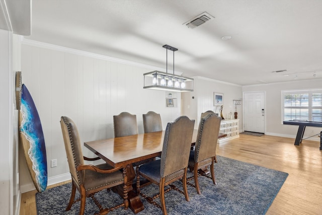 dining space featuring light hardwood / wood-style floors, ornamental molding, and wooden walls