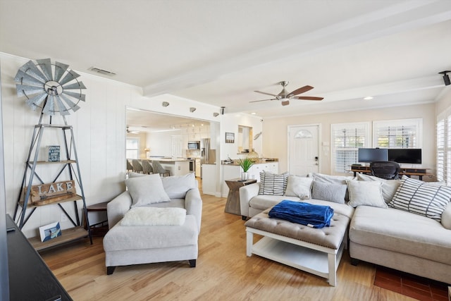 living room with ceiling fan, crown molding, beam ceiling, and light hardwood / wood-style flooring