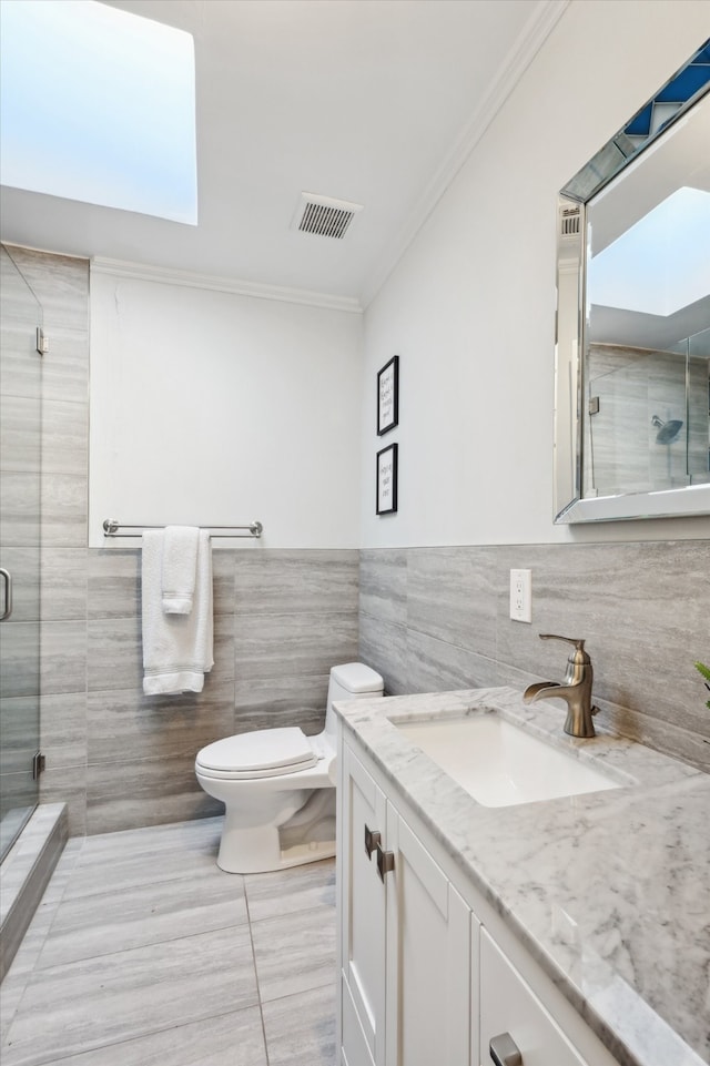 bathroom featuring a shower with door, toilet, vanity, ornamental molding, and tile walls