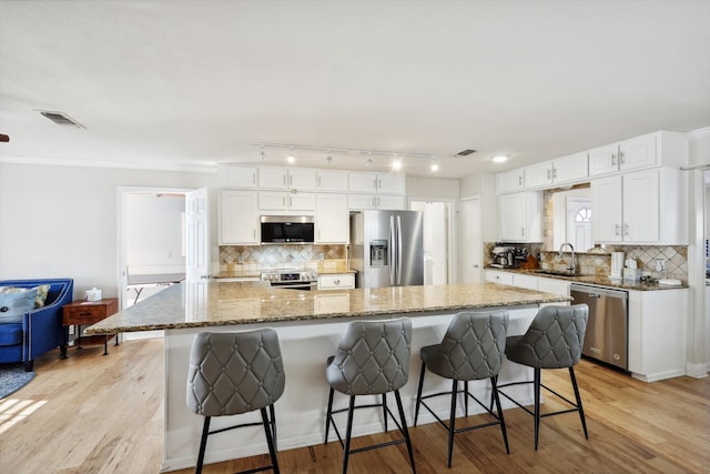 kitchen with appliances with stainless steel finishes, white cabinets, a spacious island, and light wood-type flooring