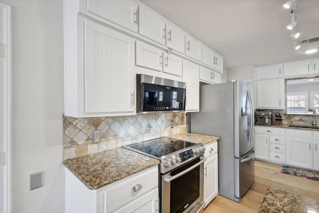 kitchen featuring appliances with stainless steel finishes, sink, white cabinetry, dark stone countertops, and light hardwood / wood-style flooring