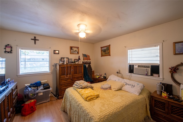 bedroom with ceiling fan, cooling unit, and light wood-type flooring