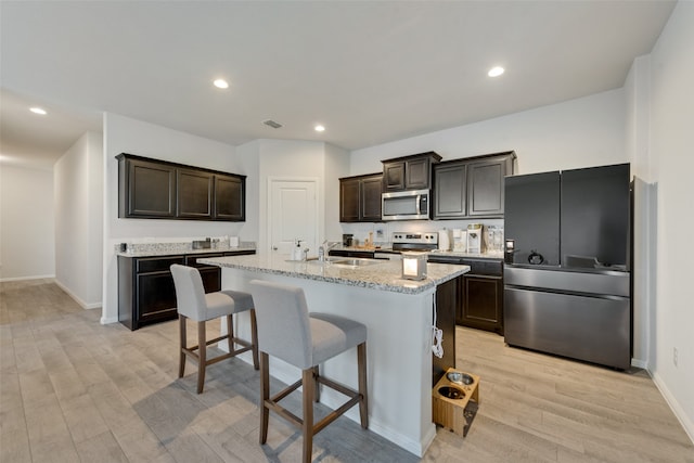 kitchen with dark brown cabinets, an island with sink, sink, light hardwood / wood-style floors, and stainless steel appliances