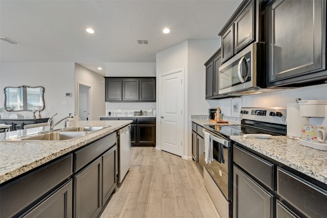 kitchen with sink, light wood-type flooring, stainless steel appliances, dark brown cabinetry, and light stone counters