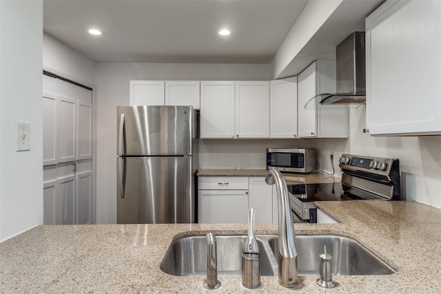 kitchen featuring light stone countertops, stainless steel appliances, wall chimney range hood, and white cabinets