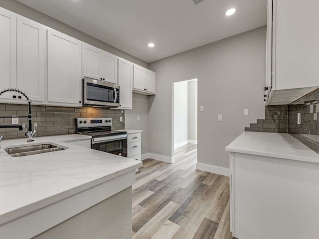 kitchen with white cabinetry, stainless steel appliances, light stone countertops, and sink