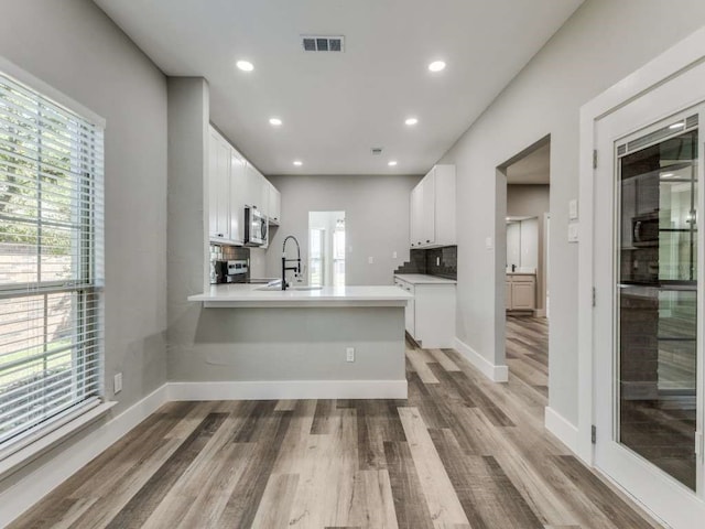 kitchen with white cabinetry, appliances with stainless steel finishes, wood-type flooring, and kitchen peninsula