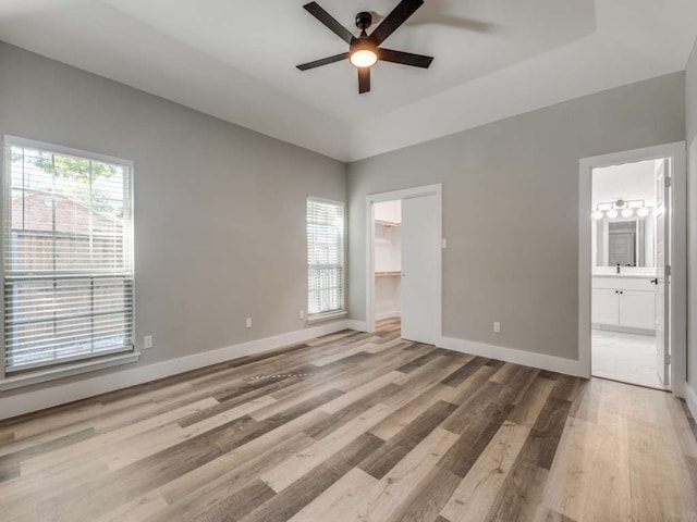 unfurnished bedroom featuring ensuite bathroom, a spacious closet, a closet, ceiling fan, and light hardwood / wood-style flooring