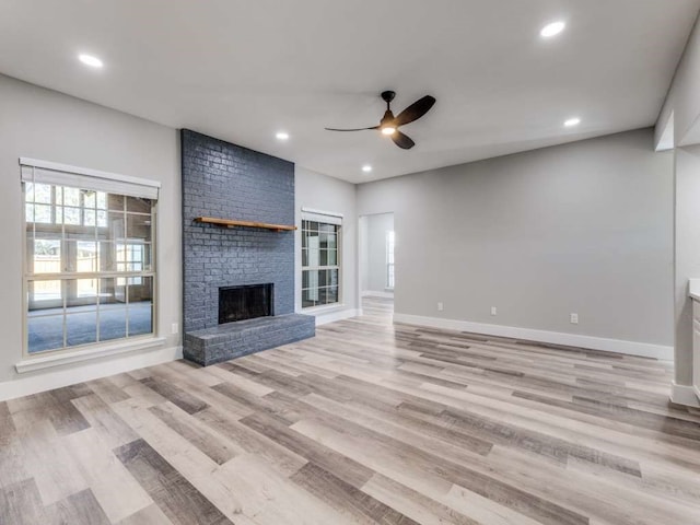 unfurnished living room featuring light hardwood / wood-style floors, ceiling fan, and a brick fireplace