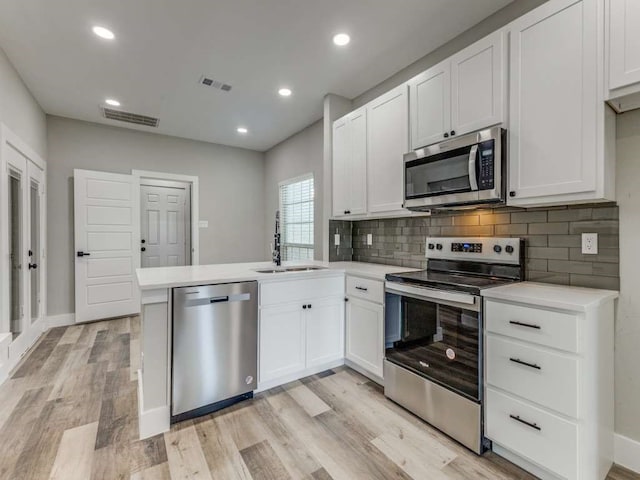 kitchen with sink, kitchen peninsula, stainless steel appliances, white cabinets, and light hardwood / wood-style flooring