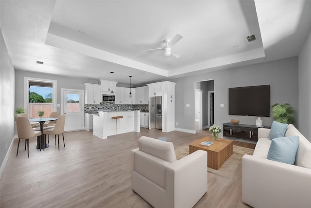 living room featuring ceiling fan, light hardwood / wood-style floors, and a raised ceiling