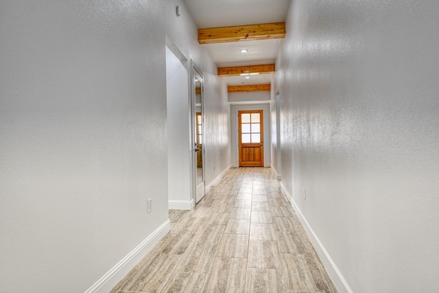 corridor with baseboards, beam ceiling, and light wood finished floors