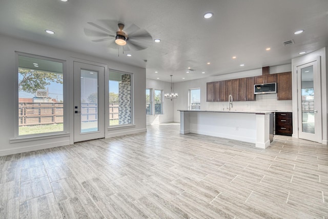 kitchen featuring light countertops, ceiling fan with notable chandelier, stainless steel microwave, open floor plan, and visible vents