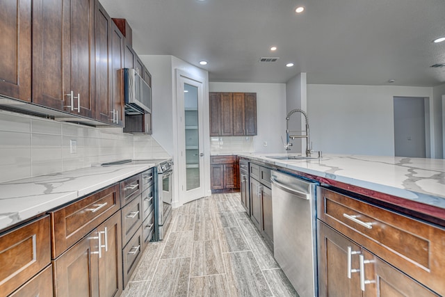 kitchen featuring light stone countertops, sink, stainless steel appliances, decorative backsplash, and light hardwood / wood-style flooring