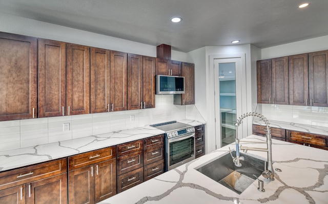 kitchen featuring backsplash, a sink, light stone counters, stainless steel appliances, and recessed lighting