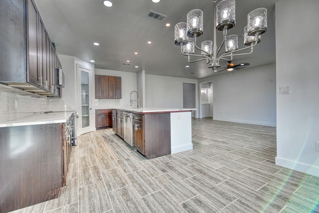 kitchen with sink, backsplash, hanging light fixtures, stainless steel appliances, and a kitchen island with sink