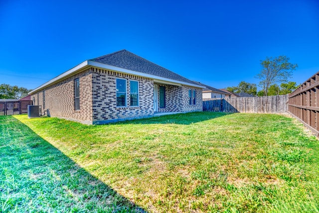 back of property featuring a fenced backyard, central AC unit, a lawn, and brick siding