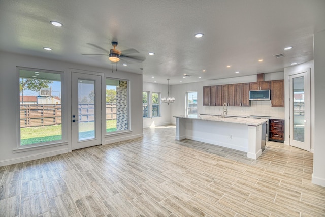 kitchen featuring open floor plan, recessed lighting, stainless steel microwave, a sink, and backsplash