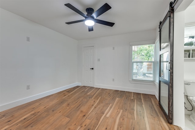 empty room featuring a barn door, light hardwood / wood-style flooring, and ceiling fan