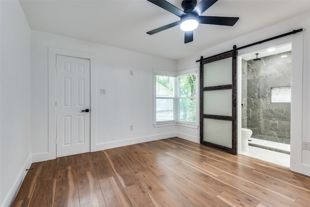 empty room featuring a barn door, light wood-type flooring, and ceiling fan