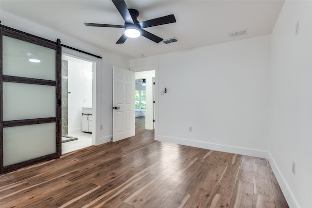 unfurnished bedroom featuring connected bathroom, hardwood / wood-style floors, a barn door, and ceiling fan