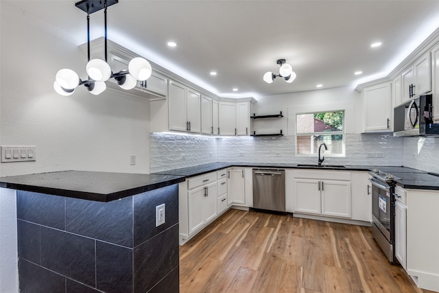 kitchen with appliances with stainless steel finishes, wood-type flooring, sink, hanging light fixtures, and white cabinets