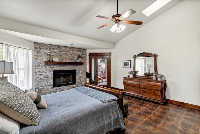 bedroom featuring dark tile patterned flooring, lofted ceiling with skylight, a stone fireplace, and ceiling fan