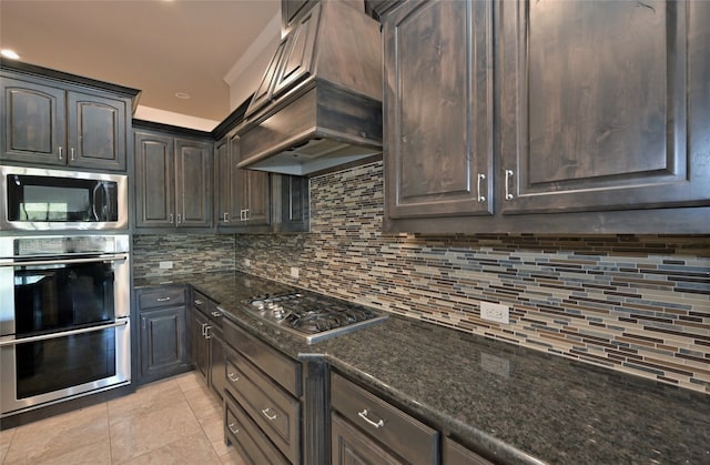 kitchen featuring custom range hood, stainless steel appliances, backsplash, dark stone countertops, and dark brown cabinetry