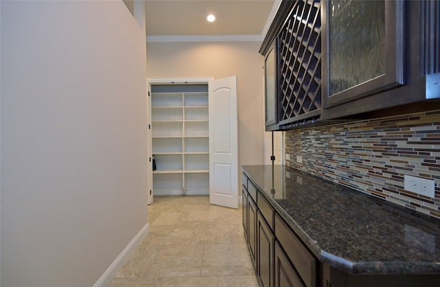 bar with tasteful backsplash, dark brown cabinets, dark stone counters, ornamental molding, and light tile patterned flooring